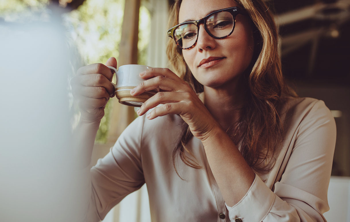 Female enjoying a cup of coffee while reading a laptop screen with a semi-neutral expression.